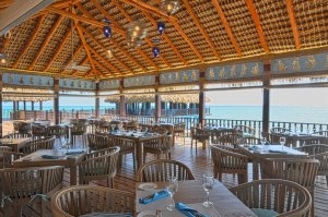 schönes offenes restaurant aus holz und bambus mit stroh dach ohne wände und gedeckten tischen am meer mit ozean blick aufs klare türkis farbene wasser mit asiatischen schriftzeichen an der decke im exotischen luxuriösen und exklusiven hotel und resort sa